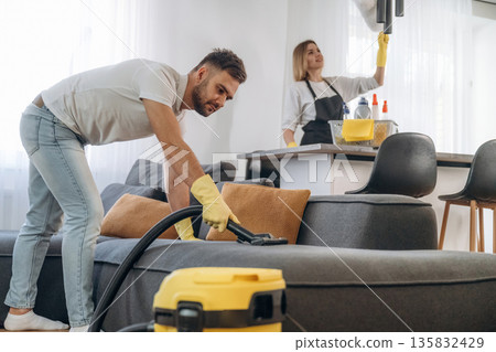Modern yellow vacuum cleaner, busy. Two cleaning service workers are in domestic room Modern yellow vacuum cleaner, busy. Two cleaning service workers are in domestic room 135832429