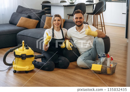 Staff sitting on floor, smiling, rest. Two cleaning service workers are in domestic room 135832435