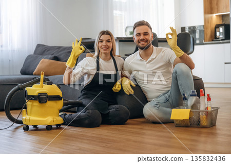 Staff sitting on floor, smiling, rest. Two cleaning service workers are in domestic room 135832436