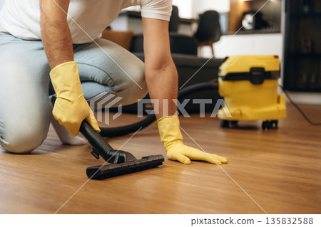 Using vacuum cleaner. Male professional cleaning service worker is domestic room Using vacuum cleaner. Male professional cleaning service worker is domestic room 135832588
