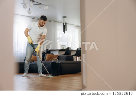 Standing and moping the floor. Male professional cleaning service worker is domestic room 135832613