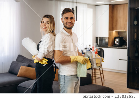 Woman is in uniform, standing. Two cleaning service workers are in domestic room 135832653