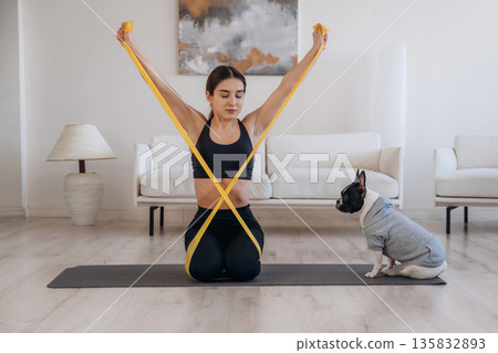 Yellow tape, stretching. Woman with pug dog is doing yoga at home Yellow tape, stretching. Woman with pug dog is doing yoga at home 135832893