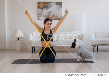 Yellow tape, stretching. Woman with pug dog is doing yoga at home Yellow tape, stretching. Woman with pug dog is doing yoga at home 135832894