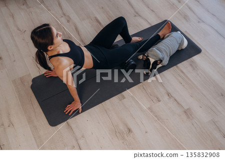 Taking a break. Woman with pug dog is doing yoga at home Taking a break. Woman with pug dog is doing yoga at home 135832908