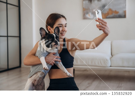 Making selfie. Sportive woman in yoga clothes is with pug dog at home Making selfie. Sportive woman in yoga clothes is with pug dog at home 135832920