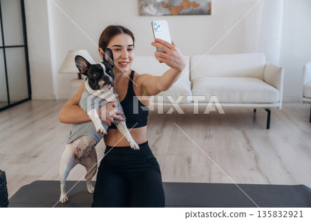 Making selfie. Sportive woman in yoga clothes is with pug dog at home Making selfie. Sportive woman in yoga clothes is with pug dog at home 135832921