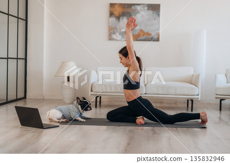 Warrior asana. Woman with pug dog is doing yoga at home Warrior asana. Woman with pug dog is doing yoga at home 135832946