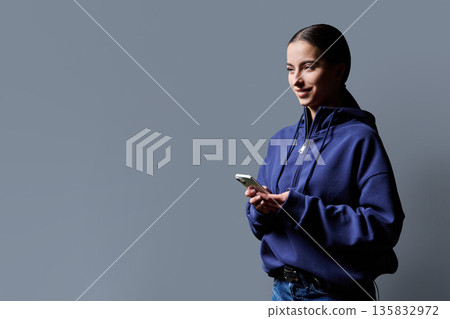 Portrait of smiling teenage girl holding smartphone on gray studio background Portrait of smiling teenage girl holding smartphone on gray studio background 135832972