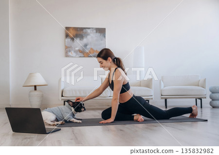 Laptop is on the floor. Woman with pug dog is doing yoga at home Laptop is on the floor. Woman with pug dog is doing yoga at home 135832982