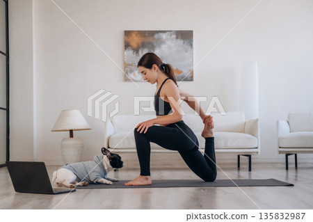 Laptop is on the floor. Woman with pug dog is doing yoga at home Laptop is on the floor. Woman with pug dog is doing yoga at home 135832987