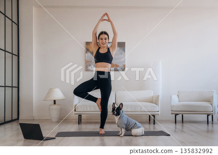 Tree exercise, standing on one leg. Woman with pug dog is doing yoga at home 135832992