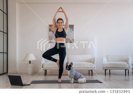 Tree exercise, standing on one leg. Woman with pug dog is doing yoga at home 135832993