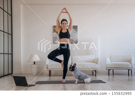Leg stand, exercise. Woman with pug dog is doing yoga at home Leg stand, exercise. Woman with pug dog is doing yoga at home 135832995
