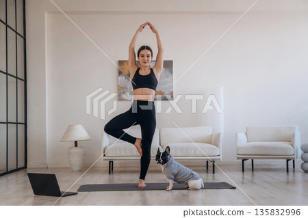 Leg stand, exercise. Woman with pug dog is doing yoga at home Leg stand, exercise. Woman with pug dog is doing yoga at home 135832996