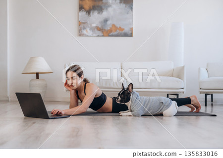 Searching the web on laptop. Woman with pug dog is doing yoga at home Searching the web on laptop. Woman with pug dog is doing yoga at home 135833016