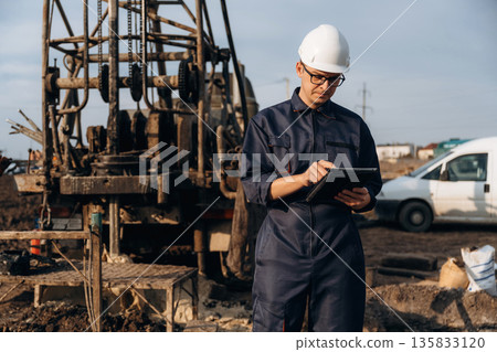 Vehicle is parked behind. Construction worker is near boring drilling machine 135833120