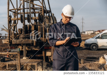 Digital tablet is in hands. Construction worker is near boring drilling machine 135833121