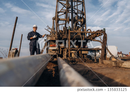 Walkie talkie in hand. Construction worker is near boring drilling machine 135833125