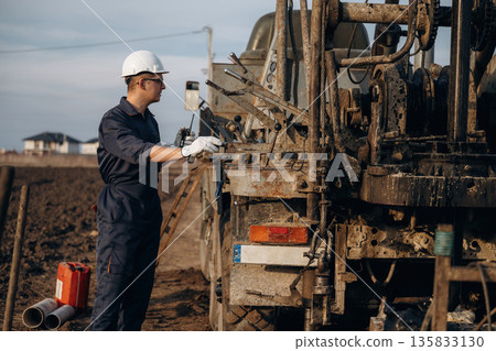 Operator is standing and making adjustments. Construction worker is near boring drilling machine Operator is standing and making adjustments. Construction worker is near boring drilling machine 135833130