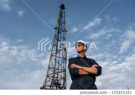 Looking to the side, arms crossed. Construction worker is near boring drilling machine 135833161