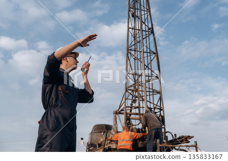 Smart guy is talking by using walkie talkie. Construction worker is near boring drilling machine 135833167