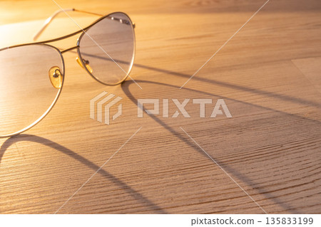 blue aviator sunglasses with large drop shaped lenses and thin metal frame. Sunglasses on light wood table casting long shadow. Summer eyewear fashion accessory with sunny highlight 135833199