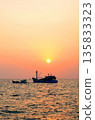 Sunset over ocean, casting orange pink colors in sky. Small fishing boats are visible in sea water 135833323