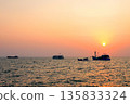 Sunset over ocean, casting orange pink colors in sky. Small fishing boats are visible in sea water 135833324