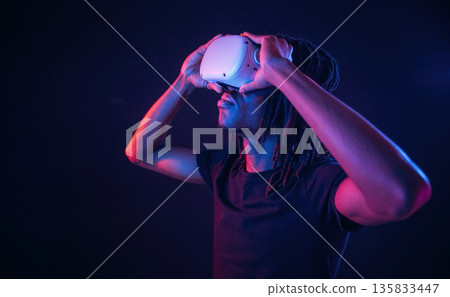Blue and red colors. African American guy is with virtual reality glasses in neon room 135833447