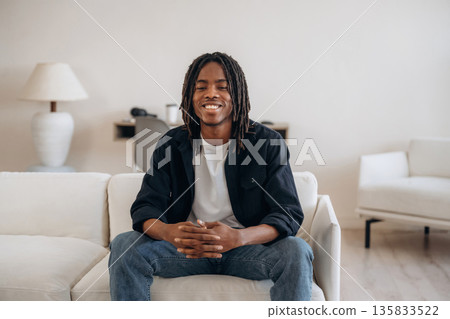 Cheerful African American guy is sitting on the sofa at home and smiling 135833522