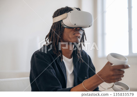 Side view, in headset. Black man in virtual reality glasses at home 135833579