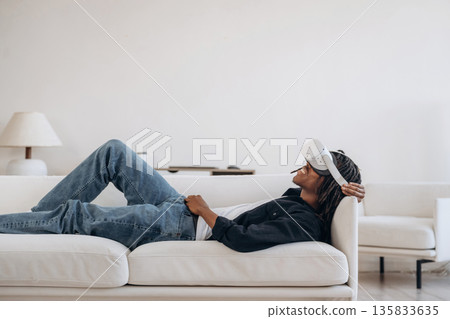 Resting, lying down and watching. Black man in virtual reality glasses at home Resting, lying down and watching. Black man in virtual reality glasses at home 135833635