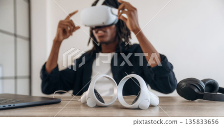 Ready for starting up. Young man is sitting by table with laptop and virtual reality glasses Ready for starting up. Young man is sitting by table with laptop and virtual reality glasses 135833656