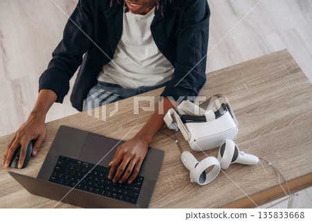 Young man is sitting by table with laptop and virtual reality glasses 135833668