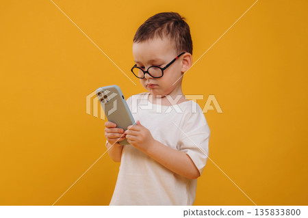Smartphone is in hands. Cute little boy is against yellow background 135833800