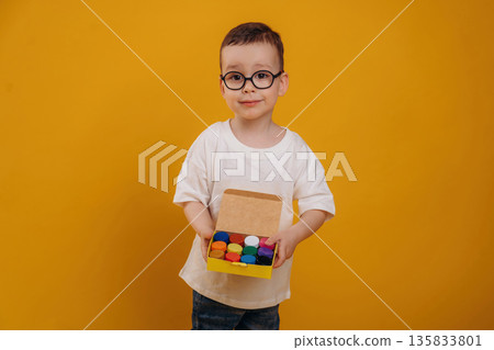 Collection of colorful paint containers. Cute little boy is against yellow background Collection of colorful paint containers. Cute little boy is against yellow background 135833801