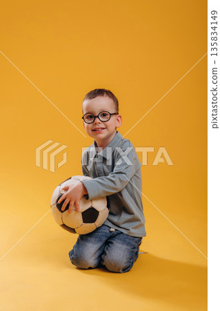 Soccer ball in hands. Cute little boy is against yellow background Soccer ball in hands. Cute little boy is against yellow background 135834149