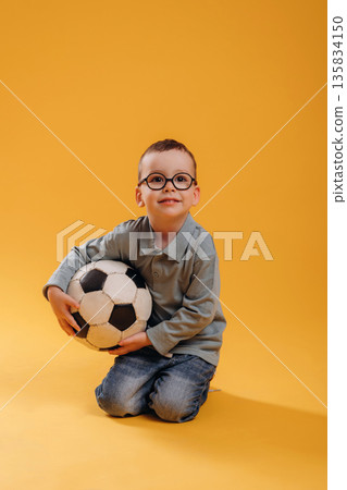 Soccer ball in hands. Cute little boy is against yellow background Soccer ball in hands. Cute little boy is against yellow background 135834150