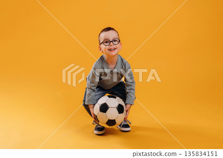 Soccer ball in hands. Cute little boy is against yellow background Soccer ball in hands. Cute little boy is against yellow background 135834151