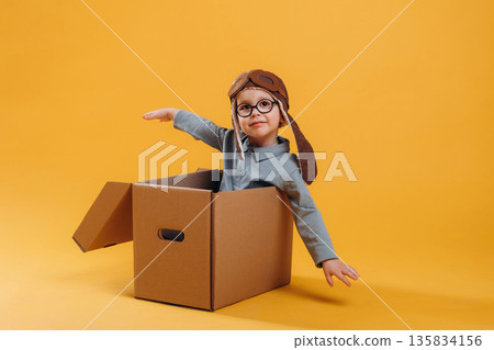 Aviator hat, in the box. Cute little boy is against yellow background 135834156