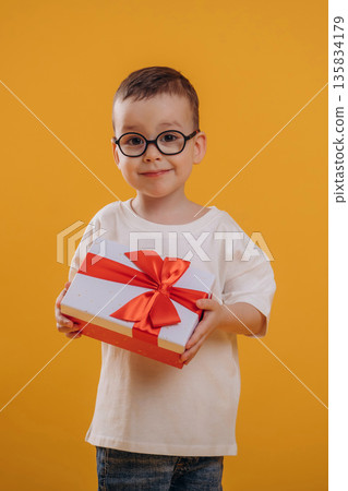 Christmas gift box, holding it. Cute little boy is against yellow background Christmas gift box, holding it. Cute little boy is against yellow background 135834179