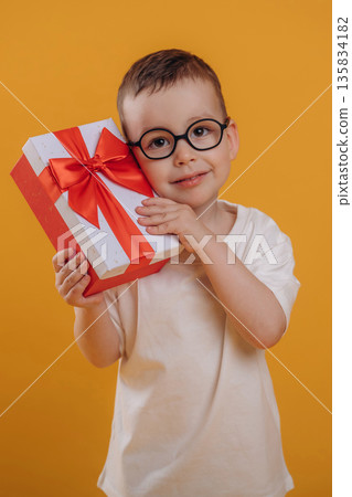 Christmas gift box, holding it. Cute little boy is against yellow background Christmas gift box, holding it. Cute little boy is against yellow background 135834182