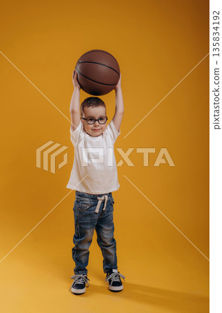 Basketball ball is in hands. Cute little boy is against yellow background Basketball ball is in hands. Cute little boy is against yellow background 135834192