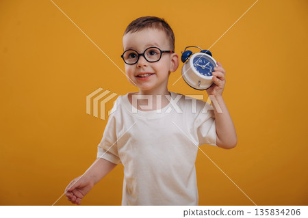 Time is running out, showing the clock. Cute little boy is against yellow background Time is running out, showing the clock. Cute little boy is against yellow background 135834206