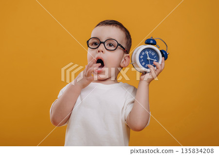 Time to sleep, holding clock. Cute little boy is against yellow background Time to sleep, holding clock. Cute little boy is against yellow background 135834208