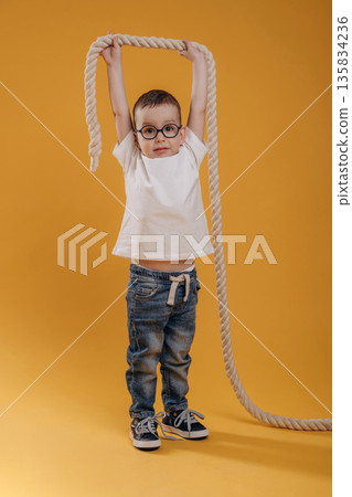 Knot is high up in hands. Cute little boy is against yellow background 135834236