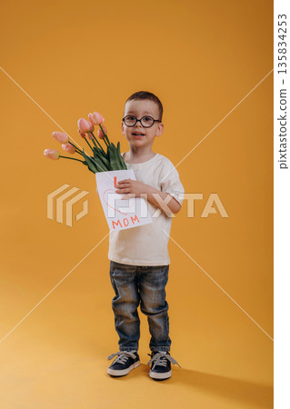 Mother's day conception, with flowers and love letter. Cute little boy is against yellow background Mother's day conception, with flowers and love letter. Cute little boy is against yellow background 135834253