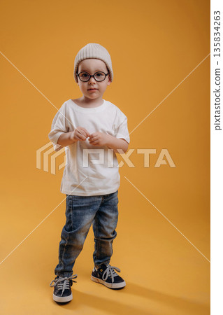 Stylish cute little boy in hat is against yellow background Stylish cute little boy in hat is against yellow background 135834263