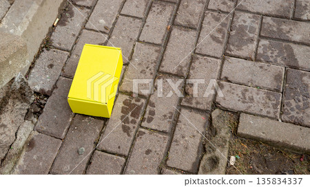 Yellow cardboard box on wet gray paving stone. Parcel, delivery, Packaging concept or misplaced item. Urban street element. Yellow cardboard box on wet gray paving stone. Parcel, delivery, Packaging concept or misplaced item. Urban street element. 135834337